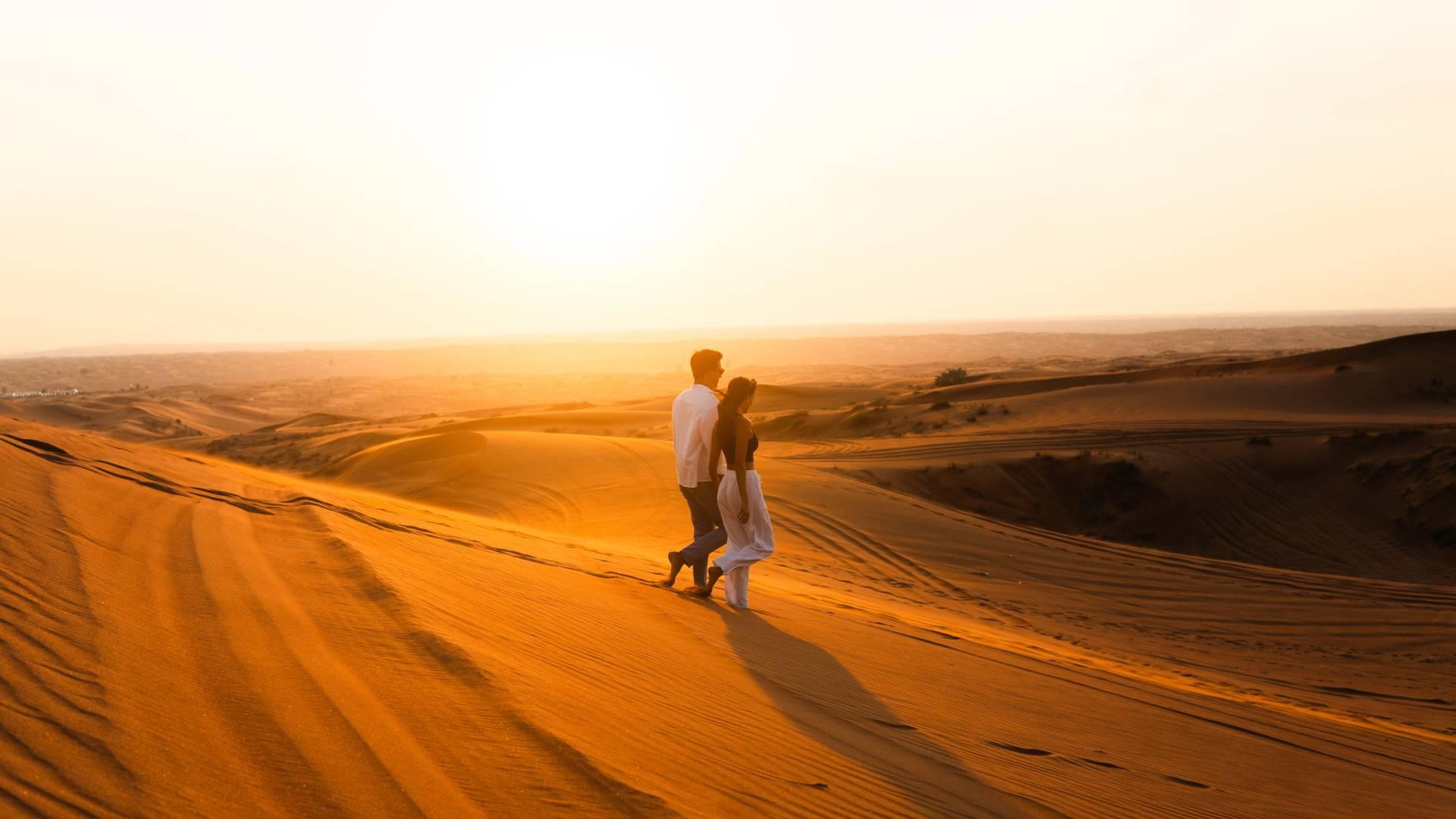 Couple walking on golden dunes during sunset at romantic desert safari in Dubai